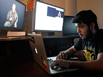 A person sitting down in the SVA editing lap working on a laptop with monitors behind them.