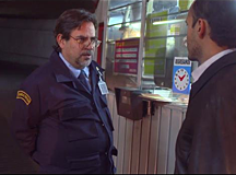 still image from Jorge Arzac's Thesis Los Medios de Intercambio. A person speaks with another person in front of a counter. The person on the left is wearing a jacket over a shirt and tie.
