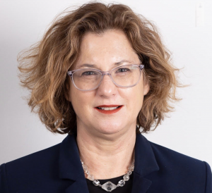 Profile photo of faculty member Kerry Fulton looking directly into the camera with a dark blazer over a dark shirt and a silver colored necklace and clear glasses.
