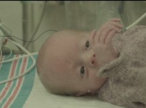 Still from Alex Kopecs film of a baby in an NICU with a blanket covering its body and cables running over it