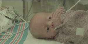 Still from Alex Kopecs film of a baby in an NICU with a blanket covering its body and cables running over it