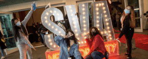Four students pose in front of a lighted neon SVA sign