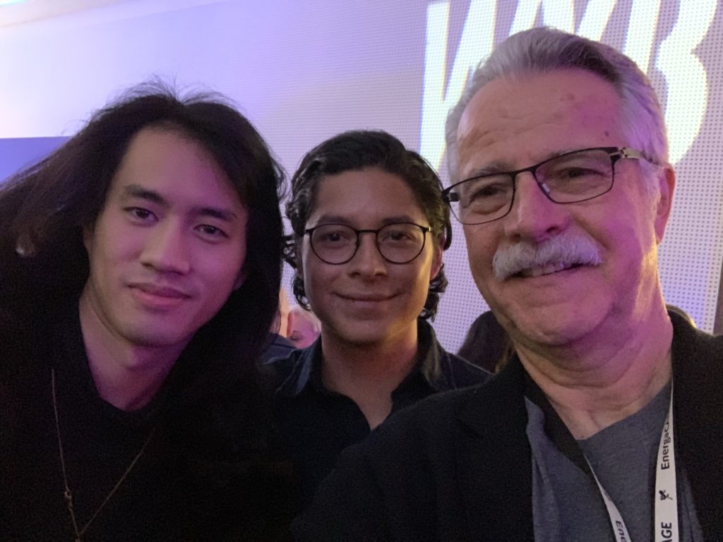 Three people pose for a group selfie. The two on the right both have glasses.