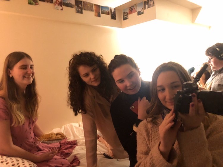 Behind the scenes still of a group of people sitting on a bed looking at a camera.