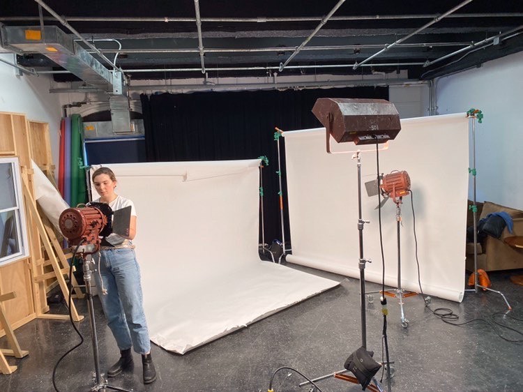 A person stands in a studio with film grip equipment all over the place. They are attending to a light fixture.
