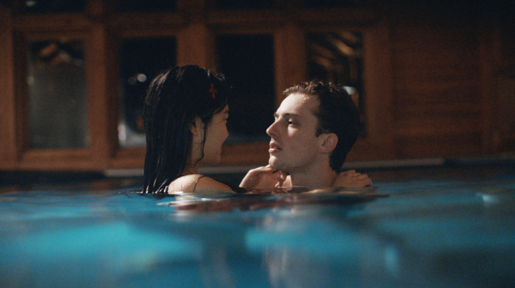 Still image from Theo Le Sourds film shows a young woman and man in a pool, close up to eachother looking one another in the eye.