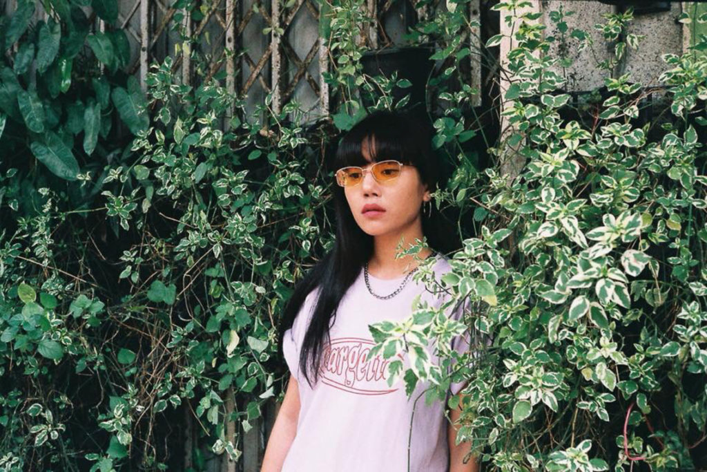 Still image of Bouquet Napursson standing in front of a building that is covered in vegetation.