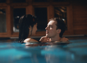 Still image from Theo Le Sourds film shows a young woman and man in a pool, close up to eachother looking one another in the eye.