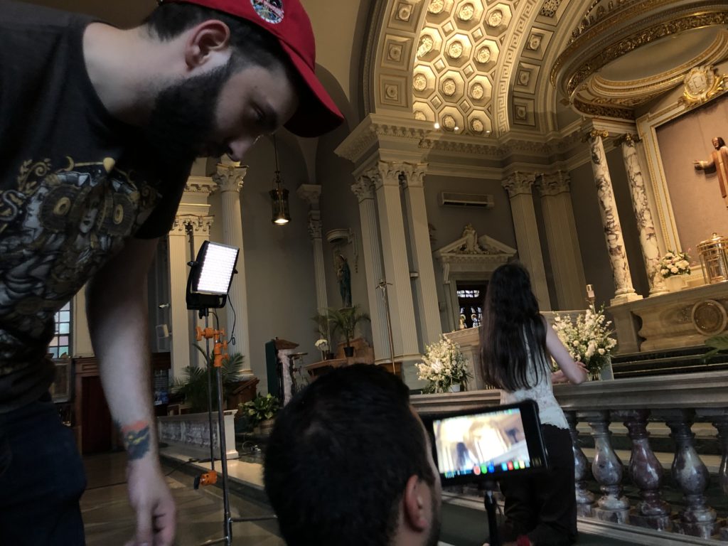 Behind the scnes of a shoot in a church. Two crew members set up a camera shot of a person praying to jesus