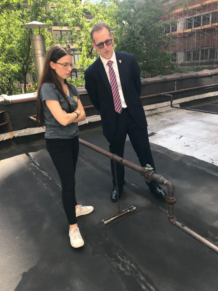 Julia Ward stands on a rooftop with an interview subject dressed in a suit and wearing glasses.