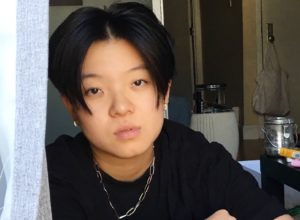 profile picture of director Meicen Meng. She stares at the camera with a black shirt and a chain around her neck.