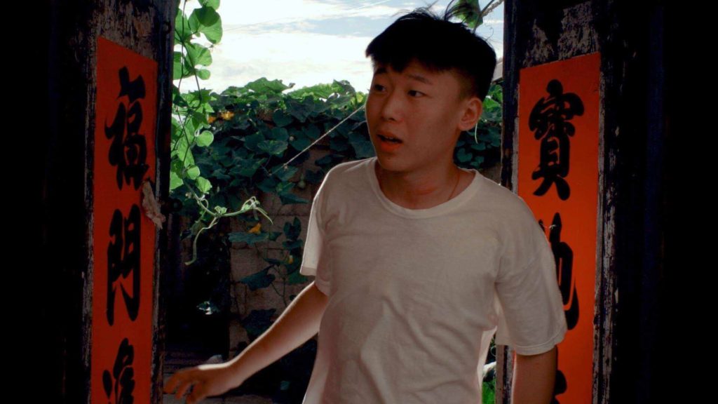 A man in a white shirt stands in the threshold of a doorway with chinese letters on the sides.