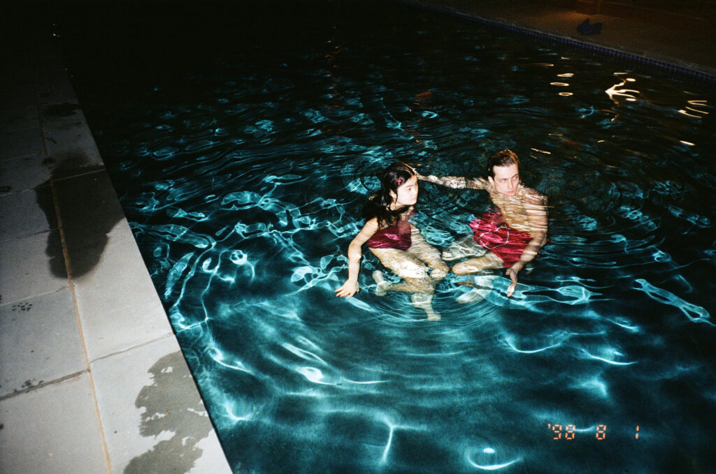 Two people standing in a shallow indoor pool. both wearing red bathing suits.