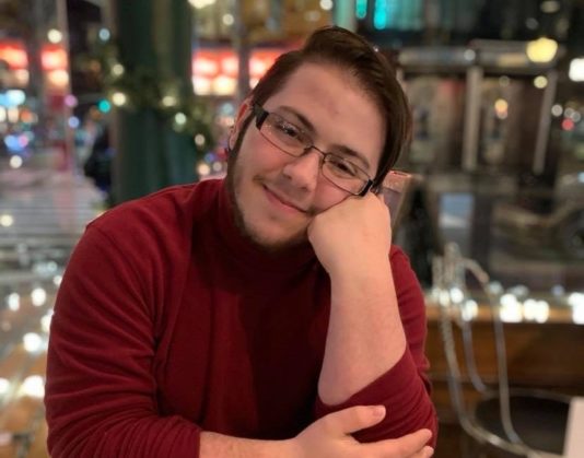 Profile photo of Flip Sarta, smiling at the camera wearing a red sweater with a blurred background of what looks like a restaurant.