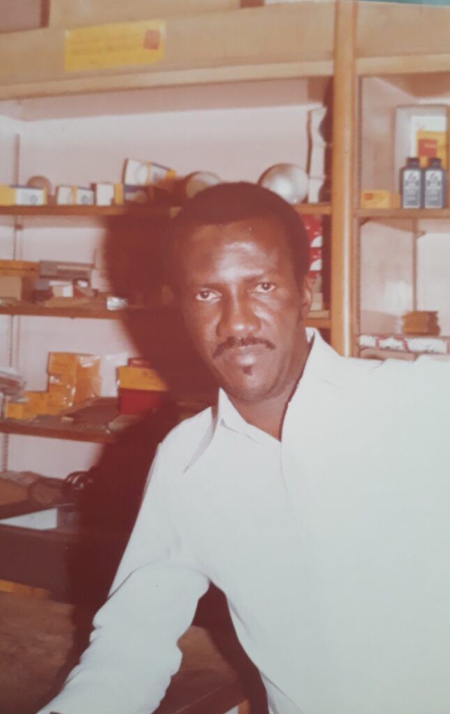 Archive photo of Sage Love's Grandfather dressed in a white button up in front of a shelf