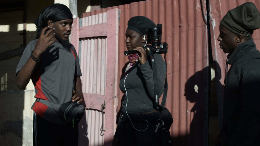 Sage Love stands next to two crew members. one of them holds a camera.