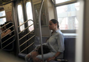 Still image from Joe Ralko's film which shows a person on the subway with someone laying next to them with their head in their lap.