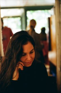 Photo of BFA Film SVA student Gonnie Zur wearing a black shirt and her right hand raised next to her ear as she looks down.