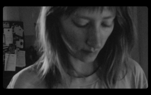 Black and white image from Gonnie Zur's film. Shows a person with shoulder length hair looking down. the image is slightly out of focus.