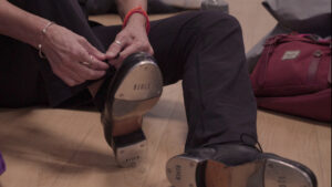 Image from Amit Lerner's film Pam. We see the hands of someone tying their shoelaces on a wooden floor.