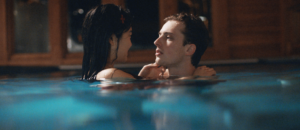 Still image from Theo Le Sourds film shows a young woman and man in a pool, close up to eachother looking one another in the eye.