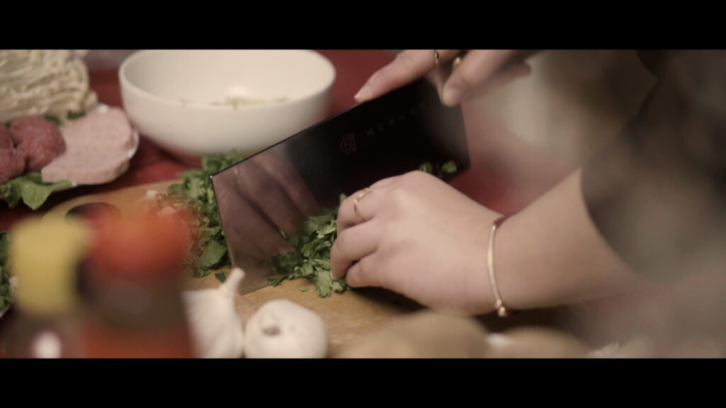 closeup image of food on a cutting board with hands and a knife chopping them.