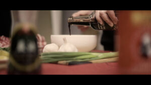 Still from Yoko Chen's short essay film shows dark soy sauce being poured into a bowl with garlic and scallions next to it