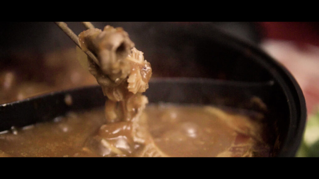 closeup photo of a chunk of food being picked out of a hotpot with a pair of chopsticks.