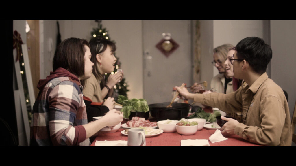 a group of people sit at a table smiling and talking while eating a hotpot meal.