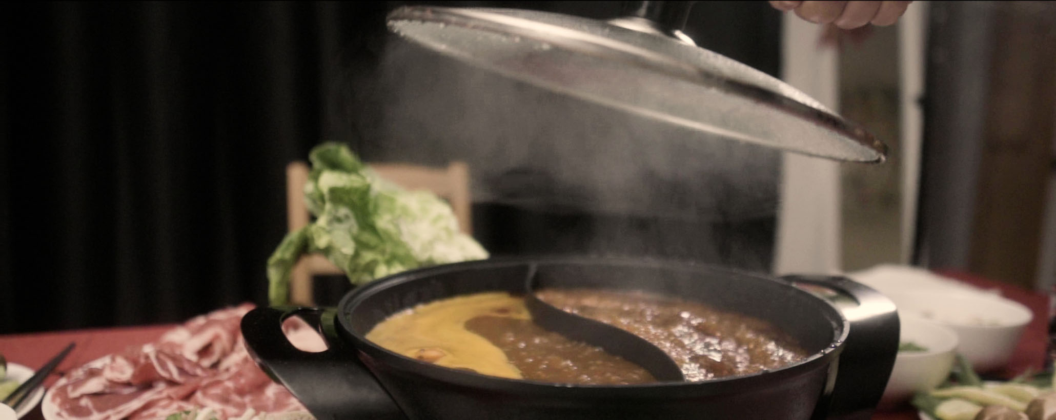 Still from Yoko Chen's short essay film shows the lid being pulled off a steaming hot pot full of food