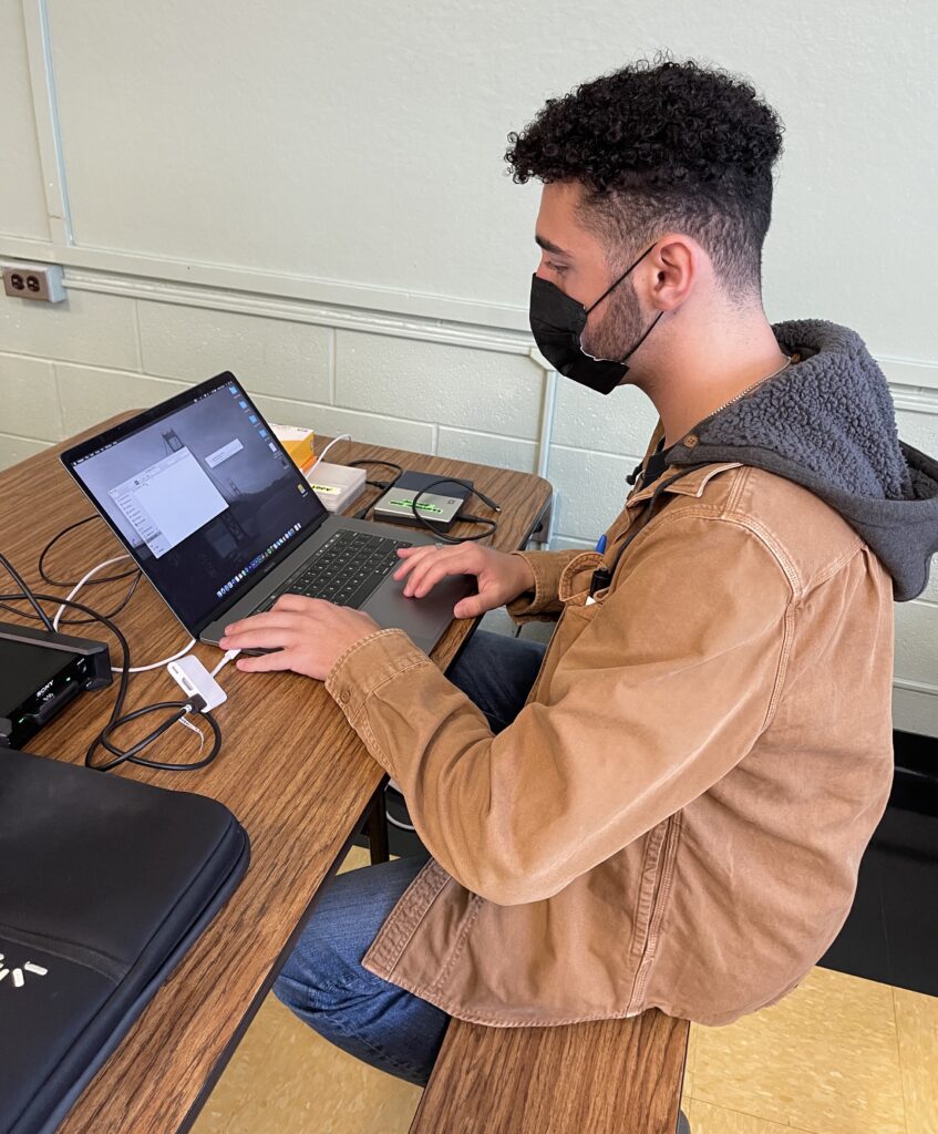 Joseph Rana working on his laptop with an external hard drive plugged in. 