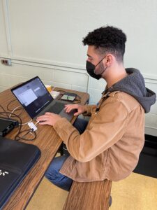 Joseph Rana working on his laptop with an external hard drive connected to it.