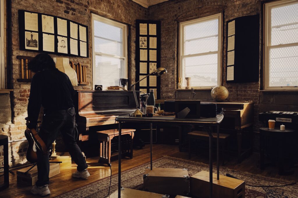 A still from Yuqing's thesis film shows someone holding a violin instrument in a room. there are also two pianos, sheet music, and other musical instruments.