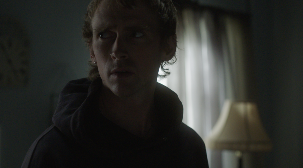 ominous photo with low lighting showing an actor from a scene in the film looking off camera inside a dimly lit apartment.