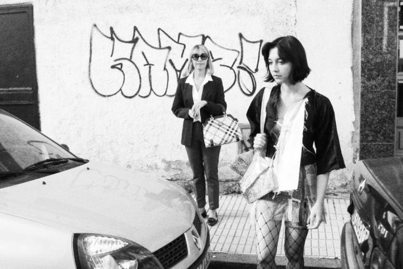 Still image of two women standing by a car