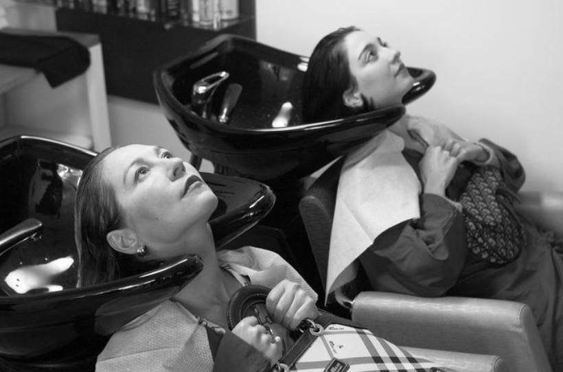 Two women sit at a hair salon getting their hair washed.
