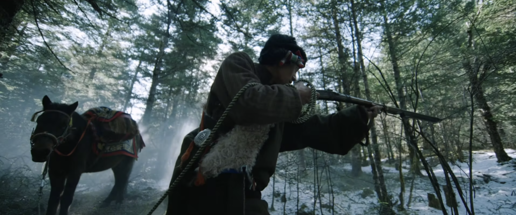 Still from Lamu's film shows a hunter holding a gun in the woods.