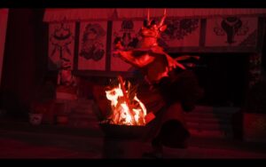 A person dressed as a red dragon dances around a red fire.