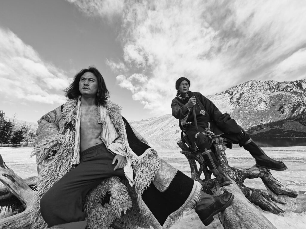 Two people pose on a fallen down tree, and behind them is a mountain.