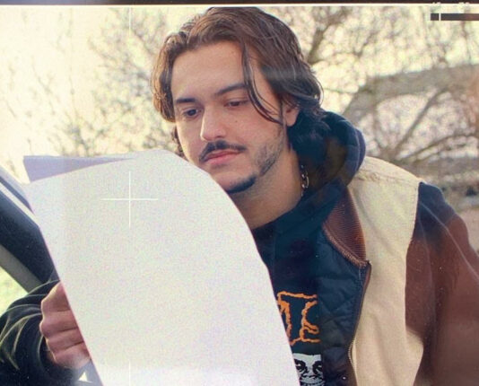 Sephen Murello stands outside with a jacket on looking at pages of a script