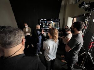 a group of people gather around a monitor as a man shows them a shot from a film