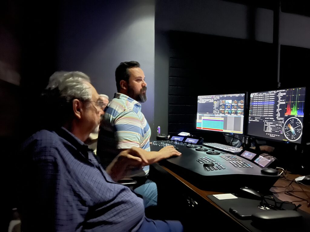 A group of filmmakers gather around a colorist working on a film in a color editing lab.