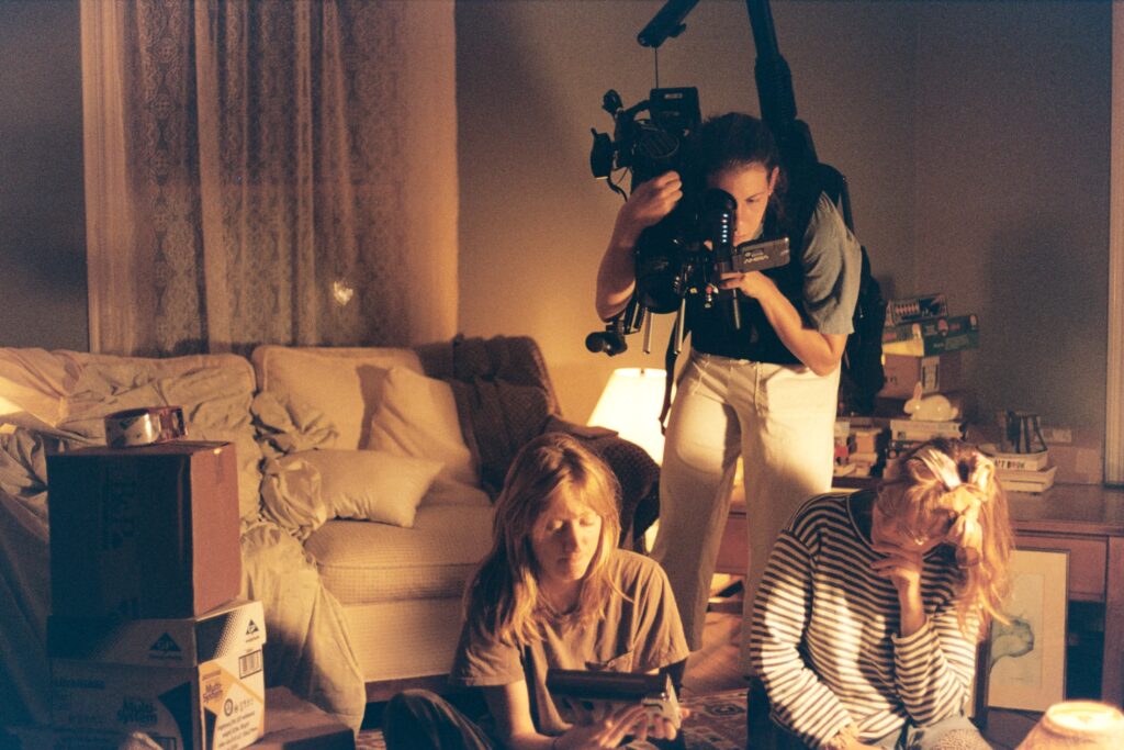 Behind the scenes image from Gonnie's film shows a cameraperson standing behind two actors sitting on the floor in an apartment set