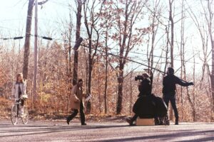 A crew filming the actor riding a bike near trees during the Fall.