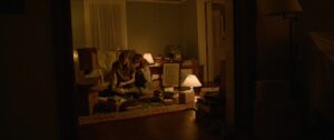 Still image from Gonnie Zur's film shows two people sitting in a living room with low lighting looking at a book.
