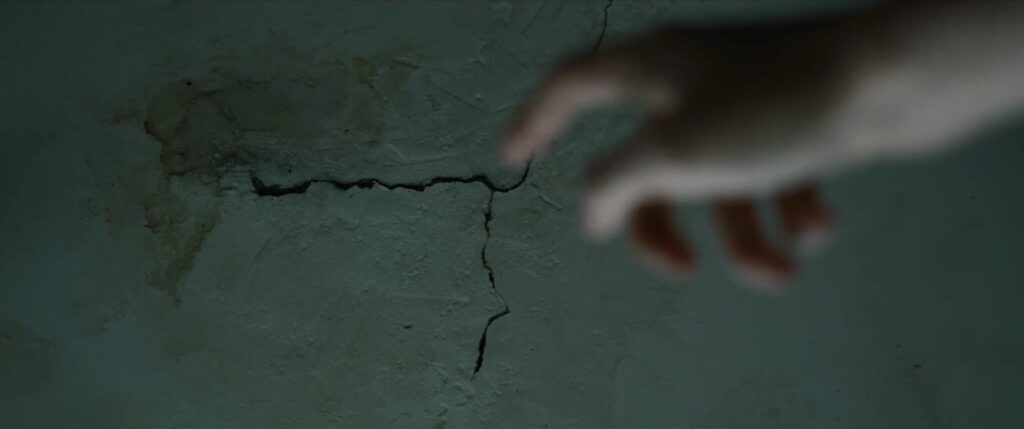 a finger points to a crack of peeling paint on a wall.