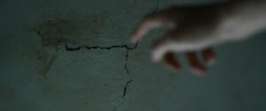 A finger pointing toward a crack in the wall.