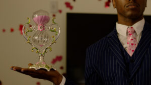 A closeup of a pink hourglass held by a well dressed person in a blue suit and a pink tie.
