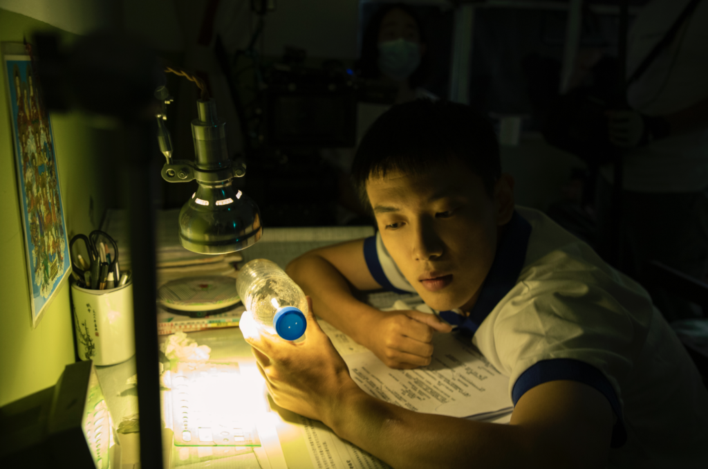 A still image from Tulpa showing a young man looking closely at a waterbottle.