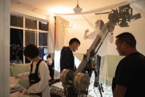 behind the scenes photo from Tulpa showing several crew memnbers setting up a shot involving a crane dolly in an apartment room set.